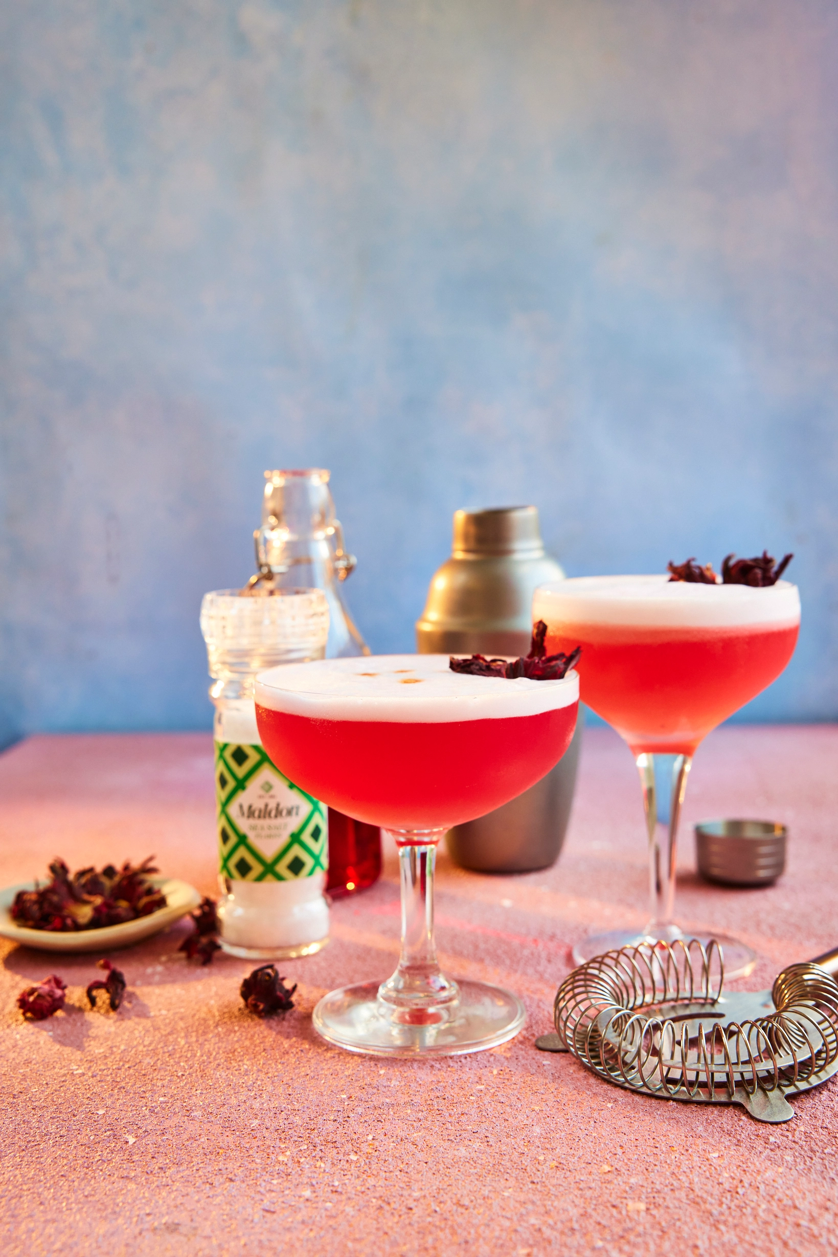 Zwei rote Cocktails mit Schaumkrone und Barzubehör
